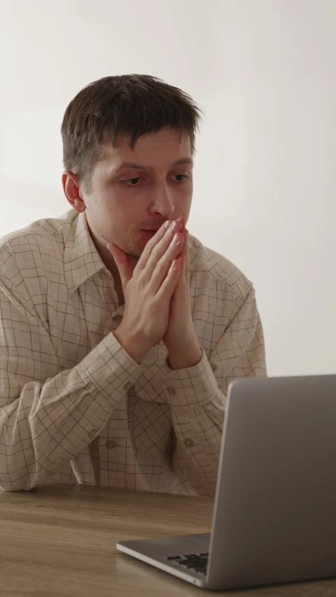 Focused young man looking at laptop screen intensely holding hands near face Stock Footage 335082332