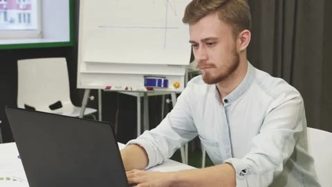 Focused young man multitasking with smartphone and laptop in a modern office Stock Footage 311951187