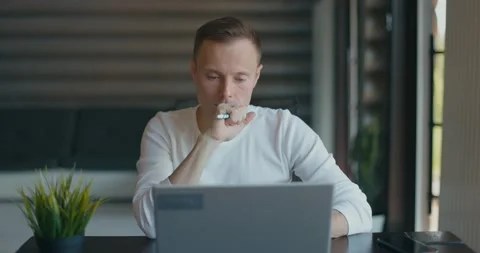 Focused young man with pen in his hand sits in room at desktop with laptop and Stock Footage 197628583