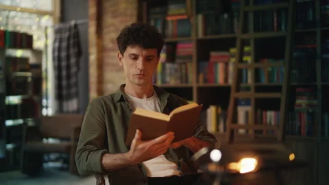 Focused young man reads book in library, enjoying literature and favorite hobby Stock Footage 342731178