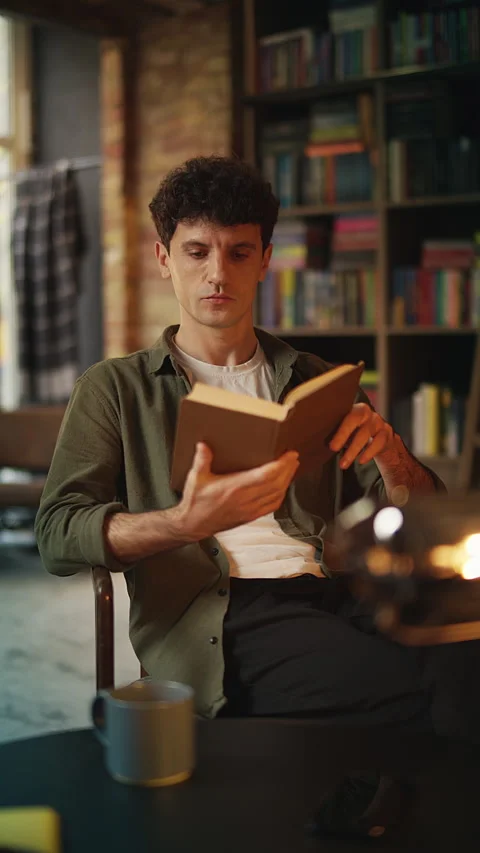 Focused young man reads interesting book in cozy bookshop cafe, enjoying hobby Stock Footage 342731788