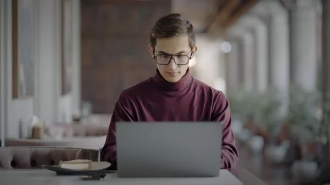 Focused young man sitting in cafe with laptop and thinking about idea of Stock Footage 343513210