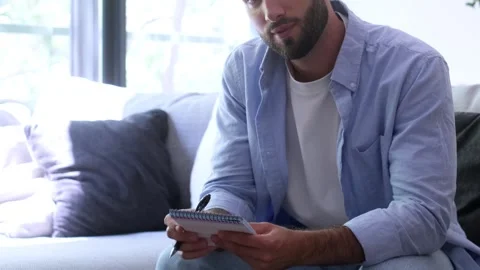 Focused young man sitting on a comfortable sofa in a modern living room Stock Footage 345078952