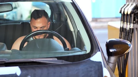 Focused young man sitting in the driver's seat of a car at a gas station Vidéo 343574539