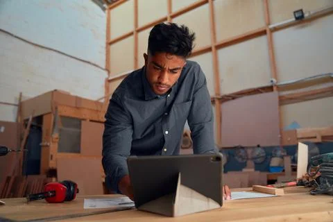 Focused young man on using digital tablet on table with ear muffs and tools in Stock Photos