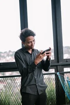 Focused young man using smartphone near window with cityscape view Stock Photos