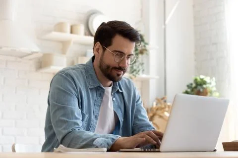 Focused young man wearing glasses using laptop, typing on keyboard Stock Photos