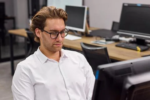 Focused young man working at computer in modern open office, wearing white shirt Stock Photos