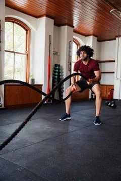 Focused young middle eastern man doing battle ropes exercises at the gym Stock Photos