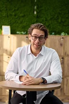 Focused young professional writing notes at desk with glasses, white shirt, warm Stock Photos