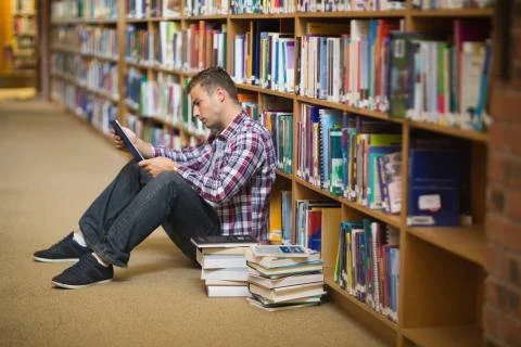 Focused young student sitting on library floor using tablet 스톡 사진
