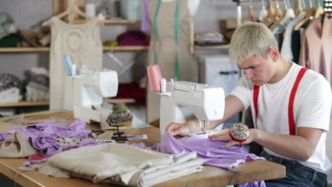 Focused young tailor sewing textile sitting at her workplace in tailor shop Stockbeeldmateriaal 332638190