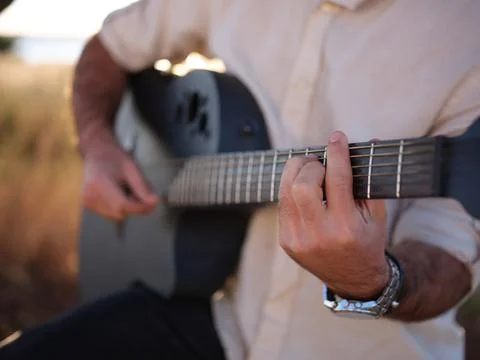 Focusing on hands while playing the guitar, male person with shirt and watch Stock Photos
