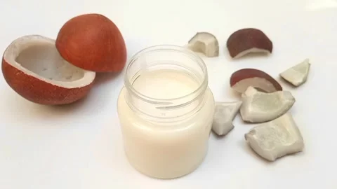 Focusing in hard coconut oil jar with split coconuts in background Stock Footage 275670341