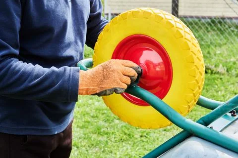 Focusing on mounting process, builder secures flat free wheel to utility ca.. Stock Photos