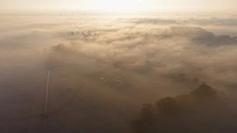 Fog blankets fields and forests at sunrise, with scattered buildings and roads Видео 328010275