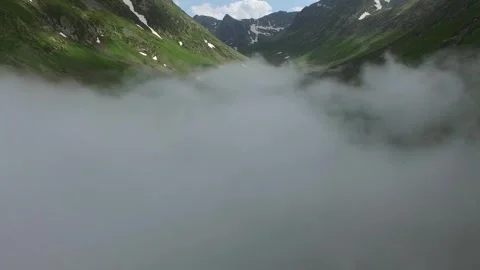 Fog blankets mountain valley with green ridges, rocky slopes, and soft daylight Stock Footage 339530308