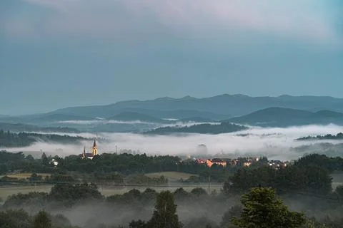 Fog coming down from mountain range to village at sunset. Stock Photos