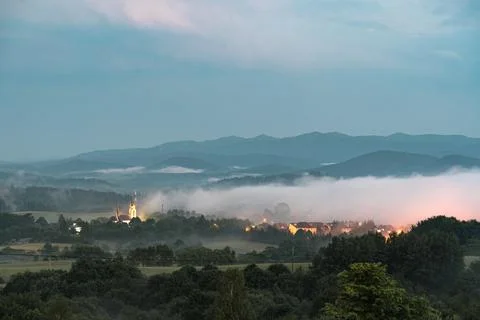 Fog coming down from mountain range to village at sunset. Stock Photos
