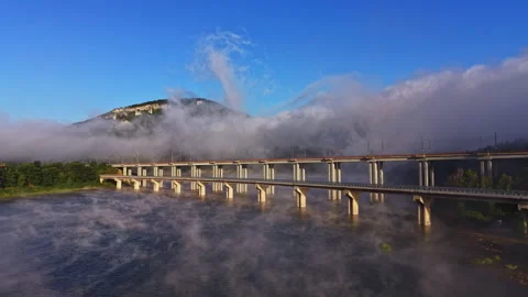Fog covers a bridge over a river with a mountain in the background during early Stock Footage 341105139