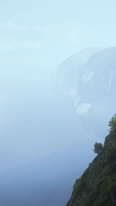 Fog covers a mountain landscape above a body of water on a clear day Stock Footage 341982410