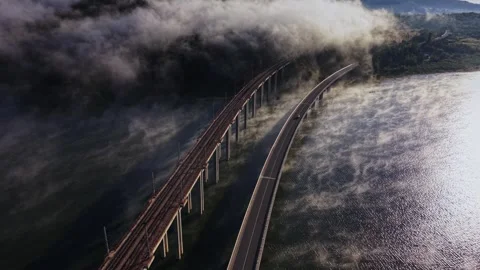 Fog covers a river and a bridge in the morning light near a mountain Stock Footage 339648274