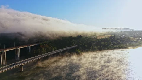 Fog covers a river and bridge at dawn with mountains in the background Stock Footage 340929821