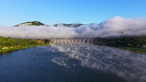 Fog covers a river and a bridge while mountains stand in the background during Stock Footage 341375738