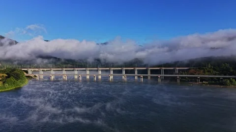 Fog covers a river near a bridge with mountains in the background Stock Footage 339648217