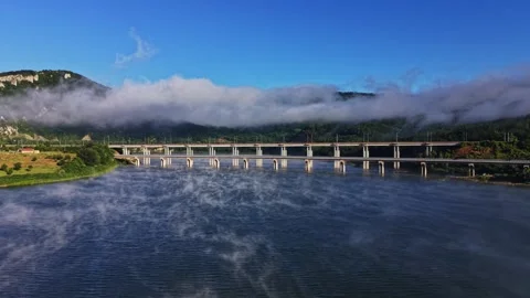 Fog covers a river under a bridge with mountains in the background Stock Footage 339648331