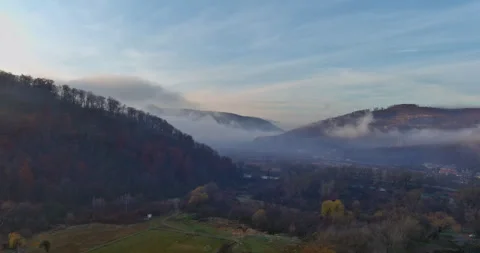 Fog drapes over hills during early morning light in serene valley landscape Stock Footage 339014136