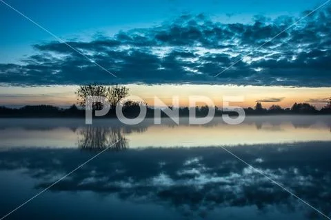 Fog on the lake, trees on the shore and clouds Stock Photos
