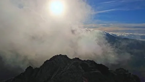 Fog moving over a rock formation at the top of a mountain, the sun shining Video stock 235823658