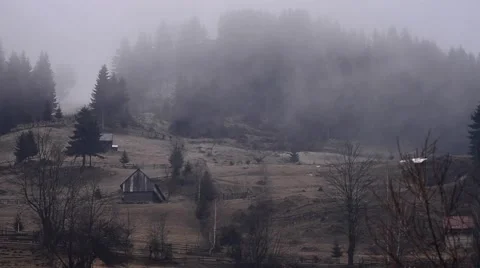 Fog passing over the dark forest on a hillside where there are several houses Stock Footage 63466428