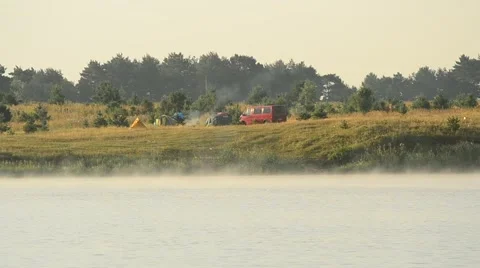 Fog rambles over a lake in summer with camp on background Stock Footage 62754076