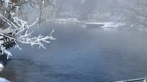 Fog rises from a clear river flowing near hoar frost covered trees Video stock 236791874