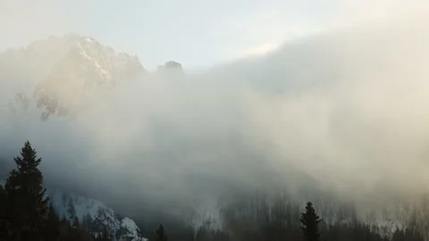 As the fog rises  a dense forest appears before snow capped rocky Italian Alps Stock Footage 225337888