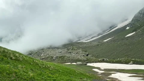 Fog rolling across an alpine slope covers rocky terrain Видео 340387782