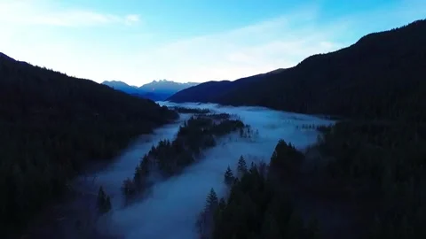 Fog rolling off a river valley with mountains in the background at sunrise Vidéo 325364248
