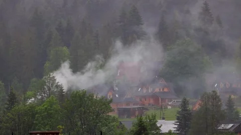 Fog rolling through a mountain forest with few visible village houses. Fogg.. Vídeos de archivo 329063839