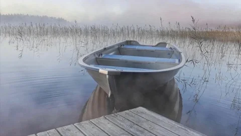 Fog rolls across still marsh with docked rowboat in still waters Stock Footage 98762905
