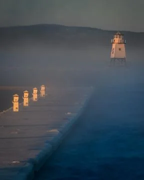 The fog rolls in at the lighthouse at dawn. Stock Photos