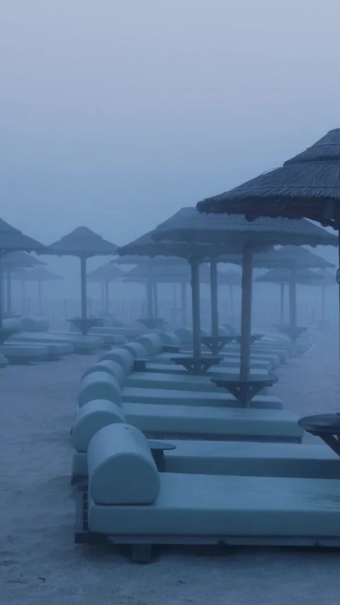 Fog slowly covering empty beach with umbrellas and lounge chairs Stock Footage 288242918