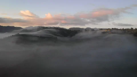 Foggy clouds wandering between hills during sunrise in New Zealand - aerial shot Video stock 153057612
