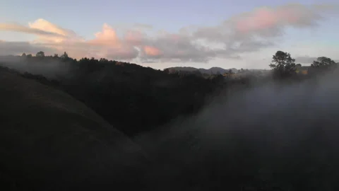 Foggy clouds wandering between hills during sunrise in New Zealand - aerial shot Video stock 153473806