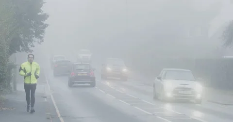 Foggy day, man in high visibility jacket jogging by busy traffic Stock Footage 146080366