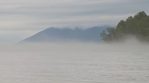 A foggy evening over the river, waves splashing on a pebble beach, in the Stock Footage 122387537