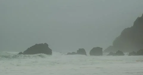 Foggy splash beach with big waves, huge rocks sticking up, cold ocean sea water Stock Footage 273407103