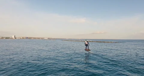A foil surfer glides gently over blue waters near the coastline Video stock 307070546