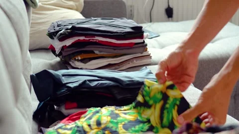 Fold clothes wardrobe on the sofa, sort through the collection of things stack. Stock Footage 295875104